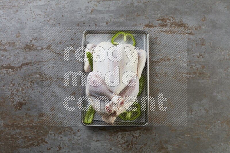 whole Raw chicken on a small oven trey direct on a rustic grey background