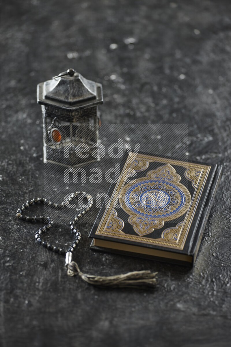 A silver lantern with different drinks, dates, nuts, prayer beads and quran on textured black background