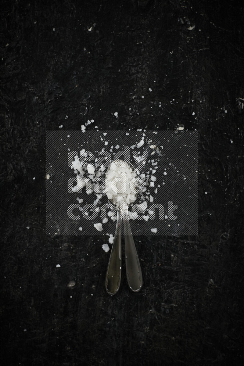 2 metal spoons filled with white salt on black background