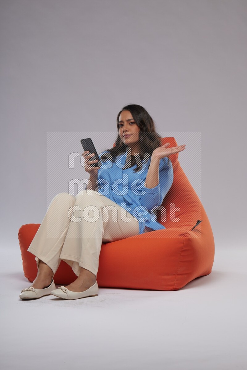 A woman sitting on an orange beanbag and texting on phone