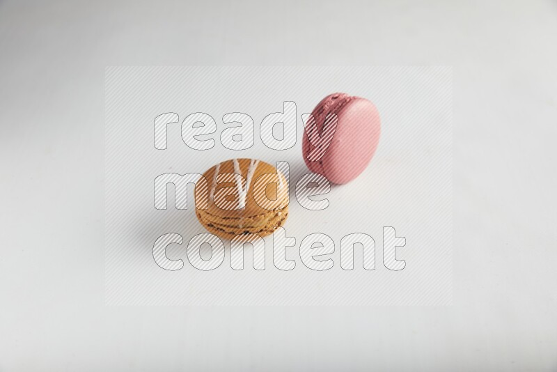 45º Shot of of two assorted Brown Irish Cream, and Pink Raspberry macarons on white background