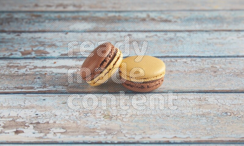 45º Shot of two Yellow and Brown Chai Latte macarons on light blue wooden background