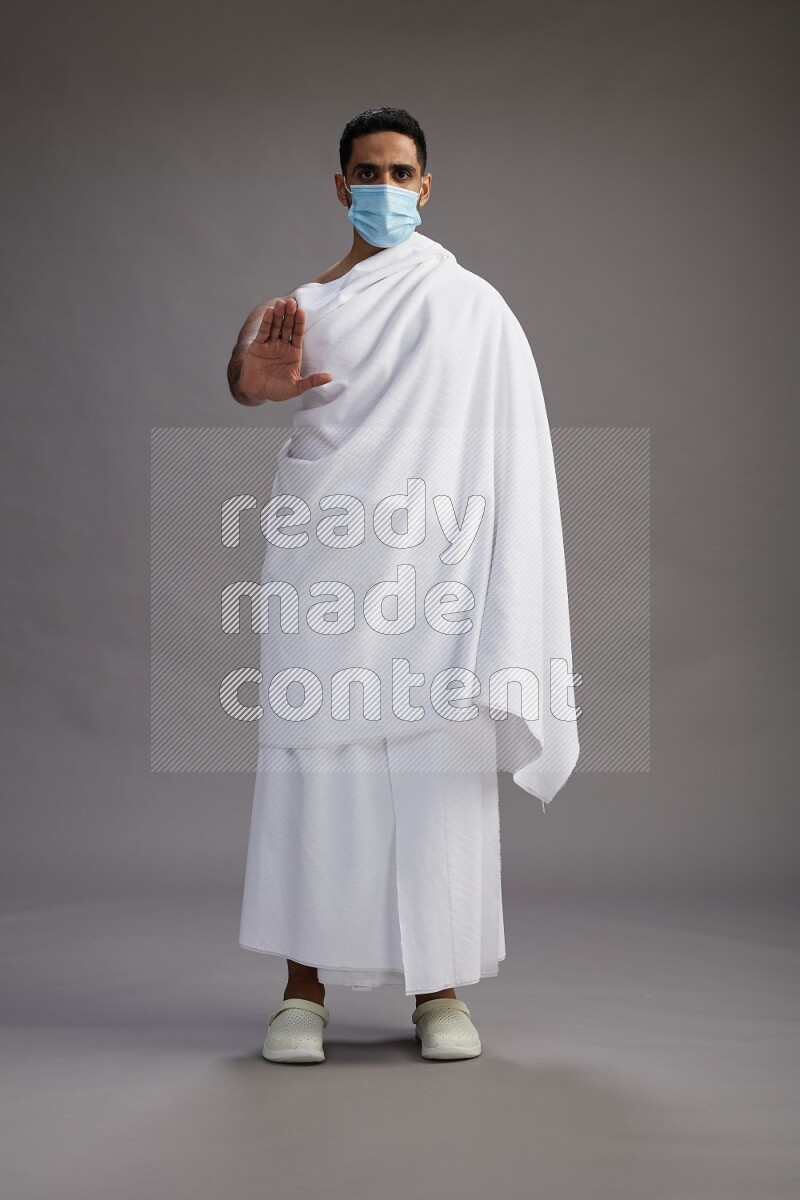A man wearing Ehram with face mask Standing Interacting with the camera on gray background