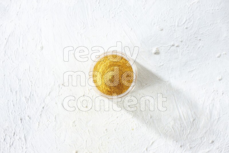 A glass jar full of turmeric powder on a textured white flooring