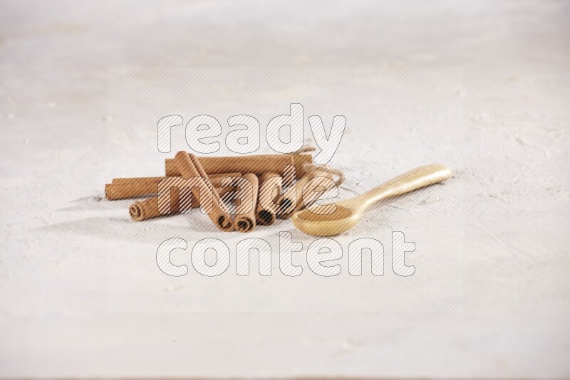Cinnamon sticks stacked beside a wooden spoon full of cinnamon powder on white background