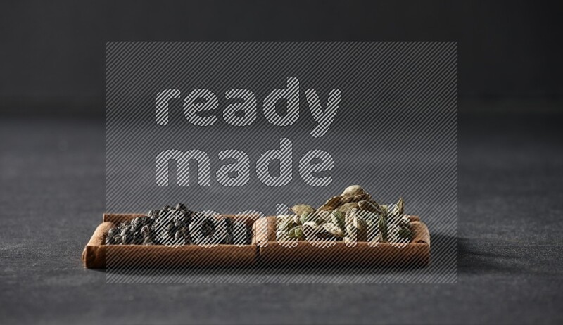 مربعان من أعواد القرفة ممتلئان بحبوب الفلفل الأسود وحب الهيل علي خلفية سوداء