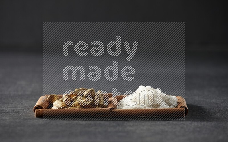 2 squares of cinnamon sticks full of white salt and turmeric fingers on black flooring