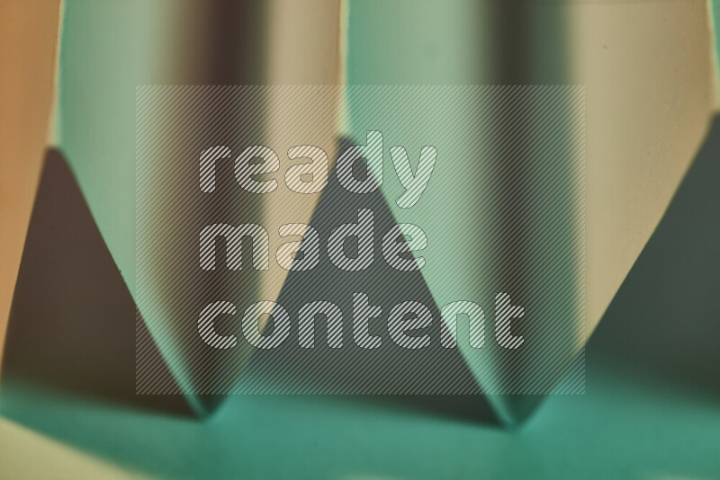 A close-up abstract image showing sharp geometric paper folds in green gradients and warm tones