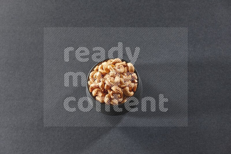 A black pottery bowl full of cashews on a black background in different angles