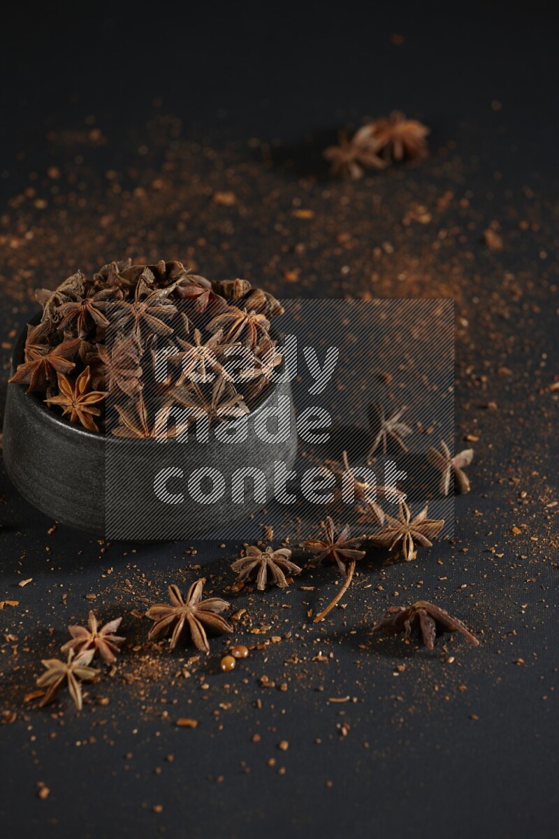 Star Anise in a black bowl with sprinkled anise on black flooring