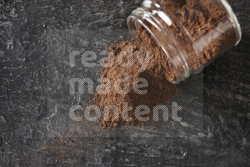 A flipped glass jar full of cloves powder on a textured black flooring