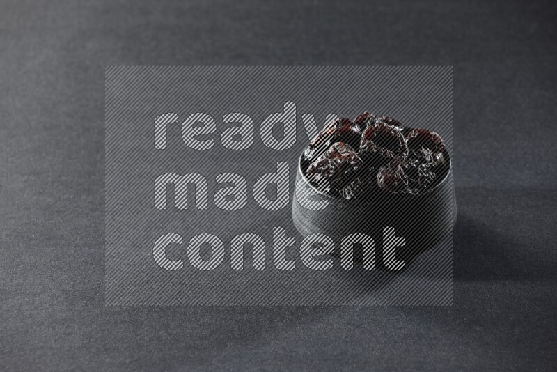 A black pottery bowl full of dried plums on a black background in different angles
