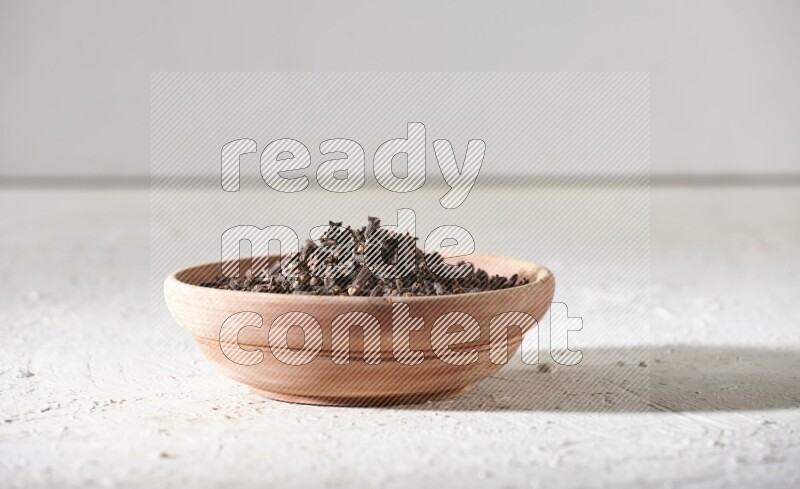 A wooden bowl full of cloves on a white flooring