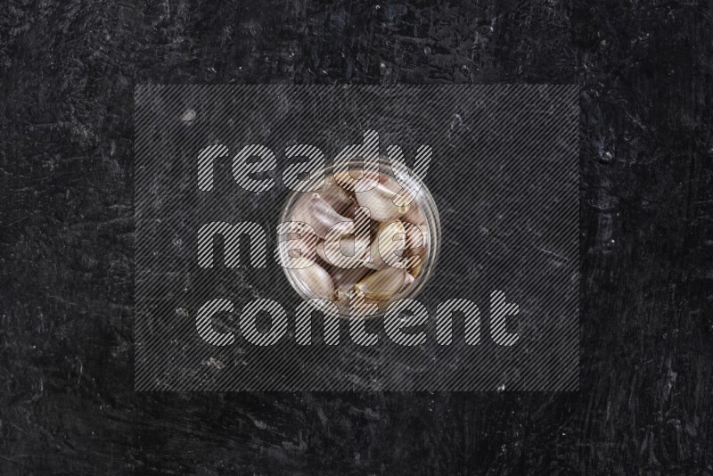 A glass jar full of garlic cloves on a textured black flooring in different angles