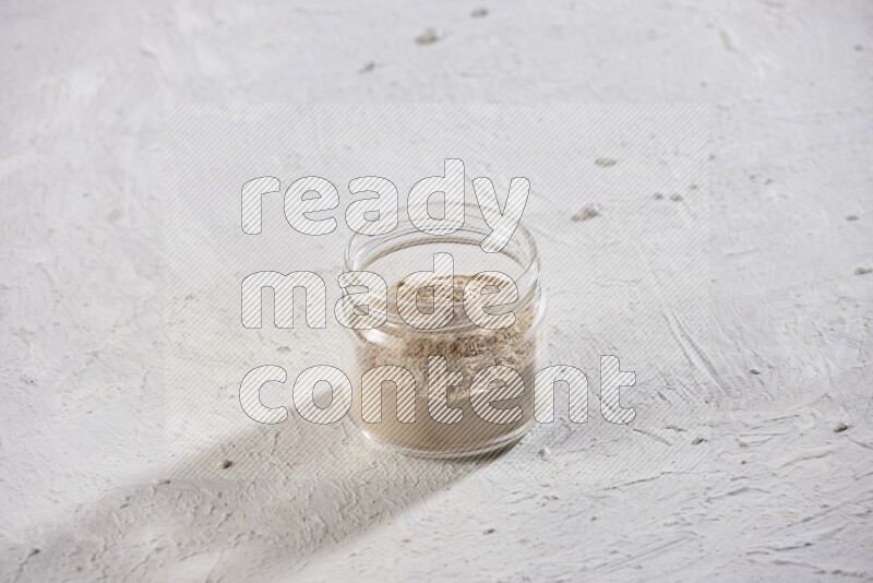 A glass jar full of garlic powder on a textured white flooring