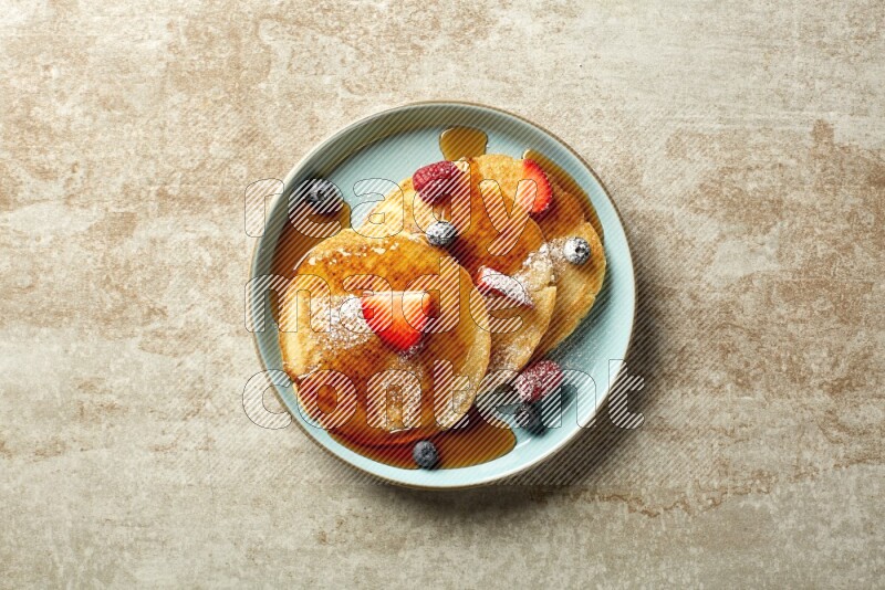 Three stacked mixed berries pancakes in a blue plate on beige background