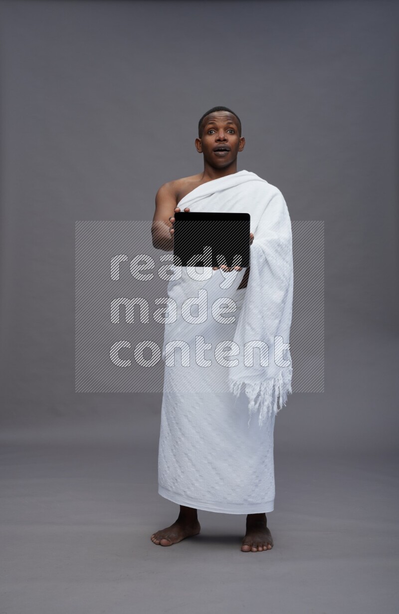 A man wearing Ehram Standing showing tablet to camera on gray background