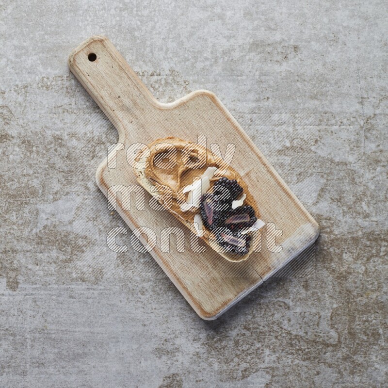 open faced peanut butter sandwich with blackberries  and coconut flakes on a  grey textured background