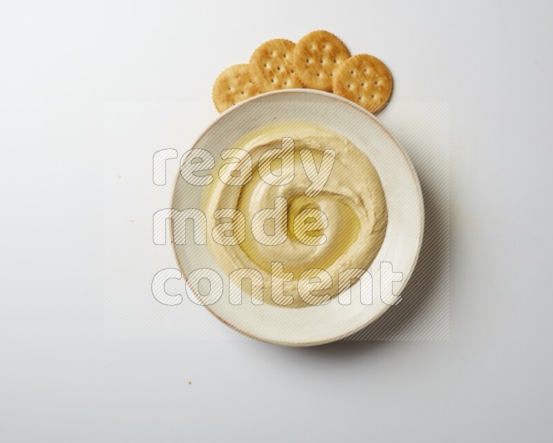 Hummus in a pottry plate garnished with olive oil on a white background