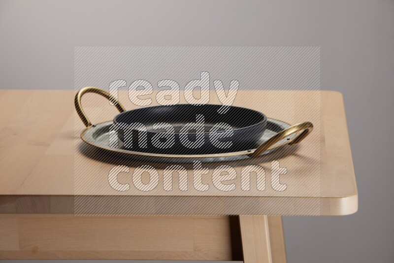 black plate placed on a rounded stainless steel metal tray with golden handels on the edge of wooden table
