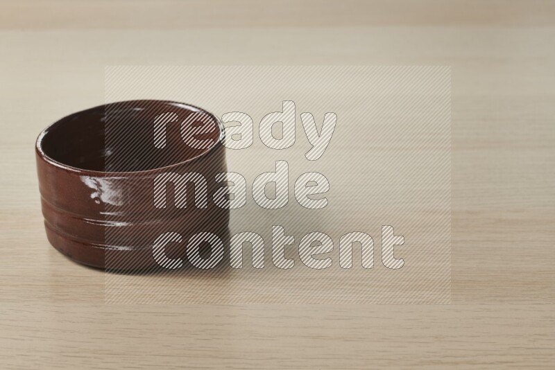 A brown pottery bowl on light wooden background
