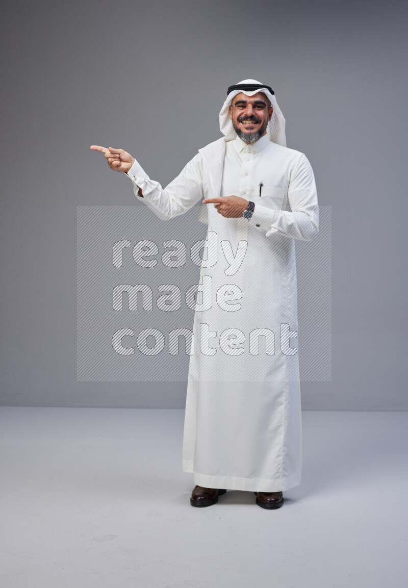Saudi man Wearing Thob and white Shomag standing interacting with the camera on Gray background