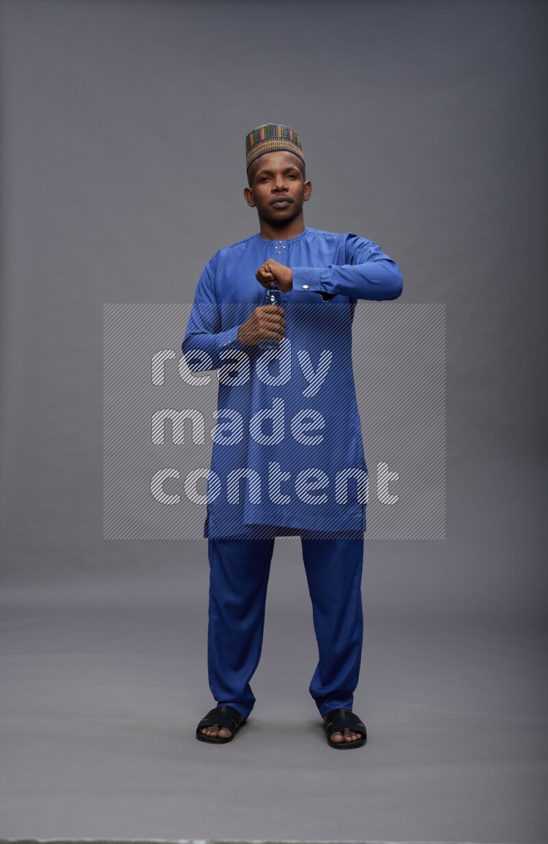 Man wearing Nigerian outfit standing drinking water on gray background