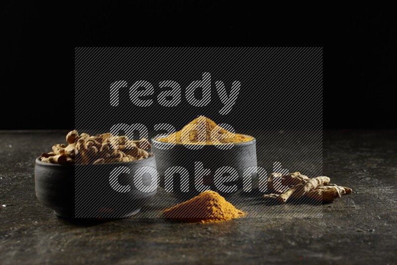 وعاءان من الفخار باللون الأسود، أحدهما ممتلئ ببودرة الكركم والآخر ممتلئ بأصابع كاملة من الكركم المجفف على خلفية سوداء