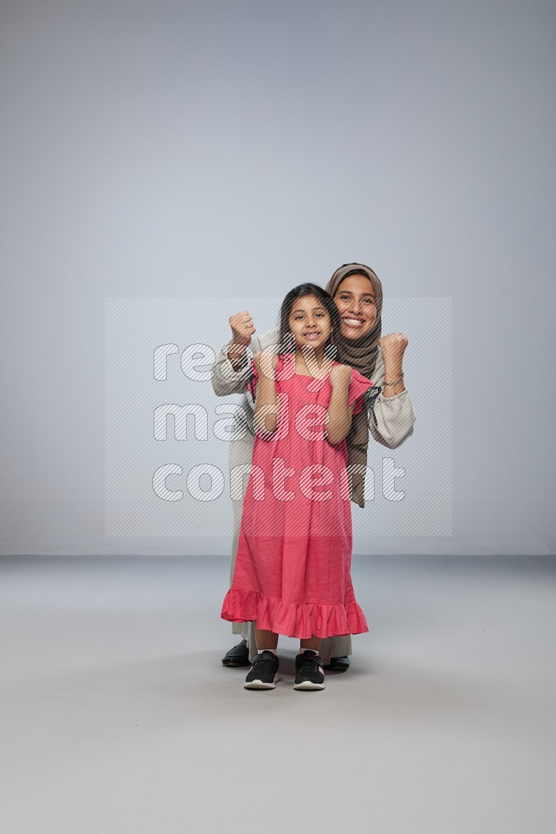 A girl and her mother interacting with the camera on gray background