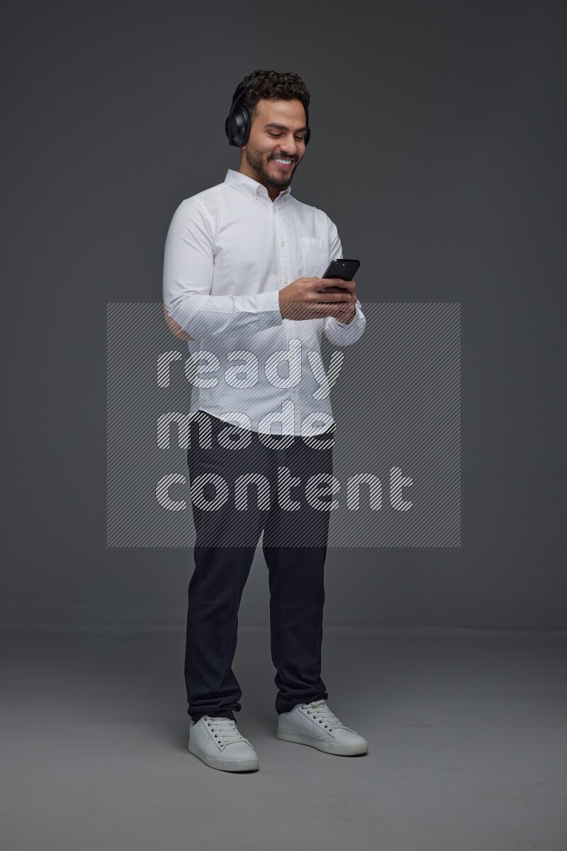 A man wearing smart casual and using his phone and headphone eye level on a gray background