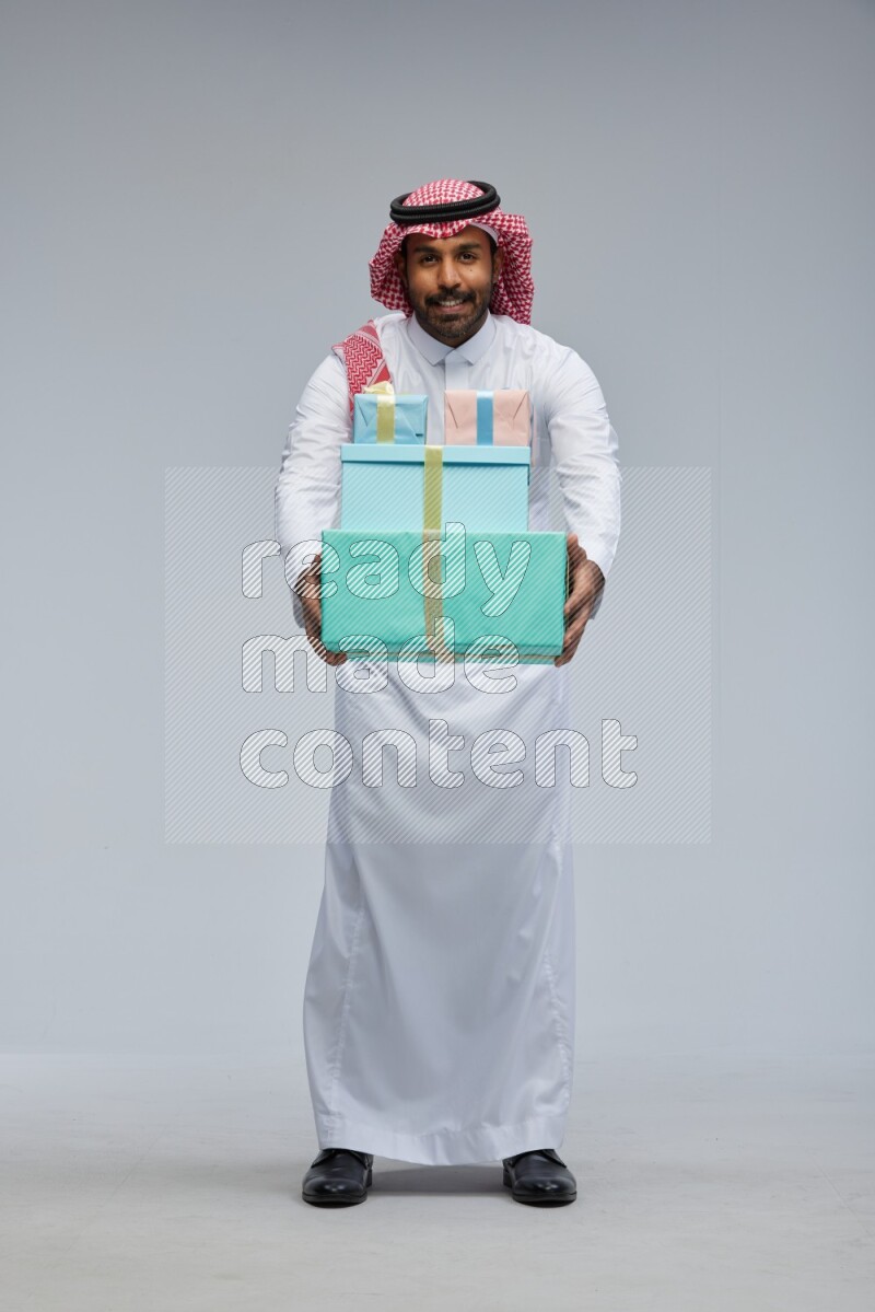Saudi man Wearing Thob and shomag standing holding gift box on Gray background