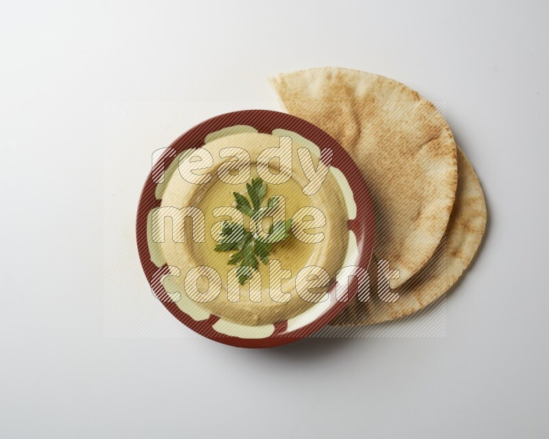 Hummus in a traditional plate garnished with parsley on a white background