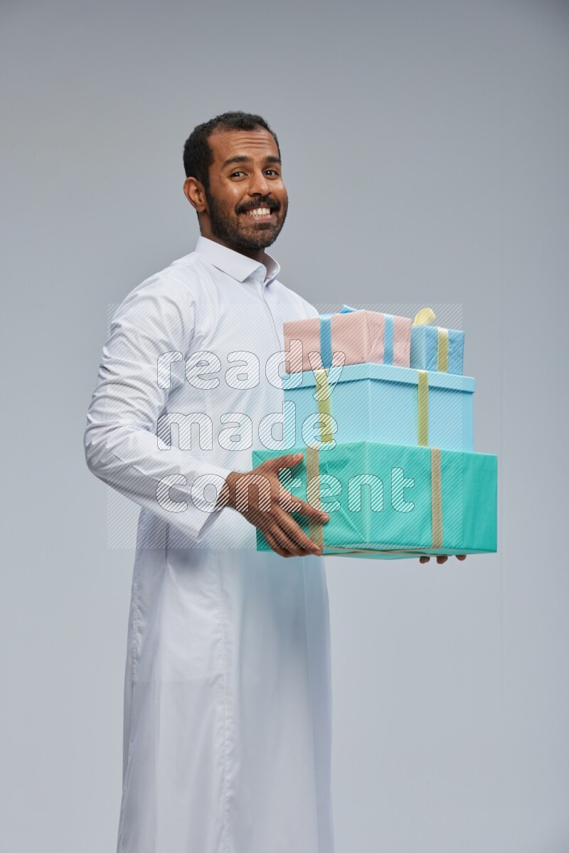 Saudi man Wearing thob standing holding gift box on Gray background