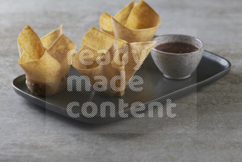 wonton cups with soy sauce ramkin on rectangle dark grey ceramic plate on grey textured counter top