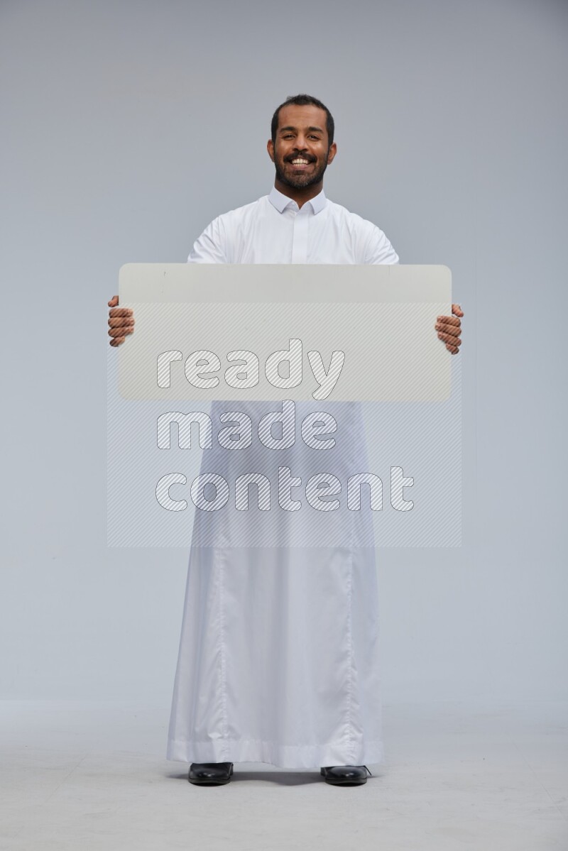 Saudi man wearing Thob standing holding board on Gray background