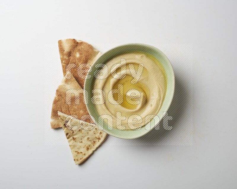 Hummus in a green plate garnished with olive oil on a white background
