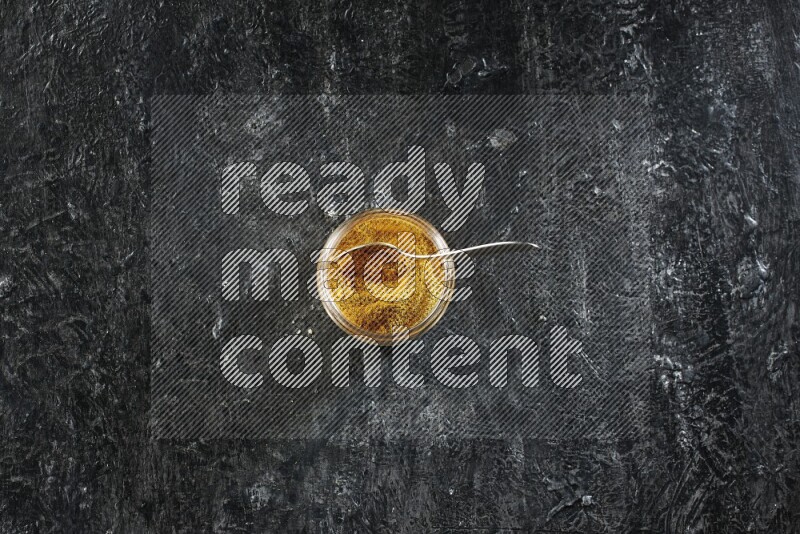 وعاء زجاجي وملعقة معدنية ممتلئان ببودرة الكركم على خلفية سوداء