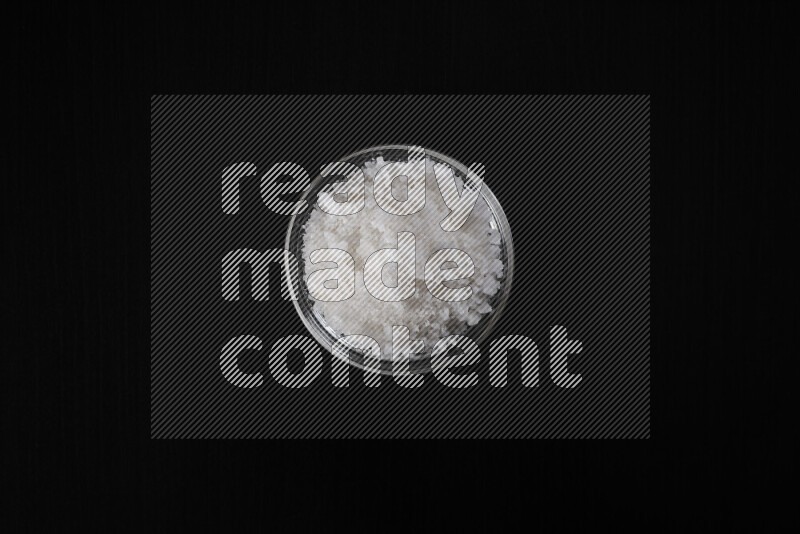 وعاء زجاجي ممتلئ بملح البحر الخشن على خلفية سوداء