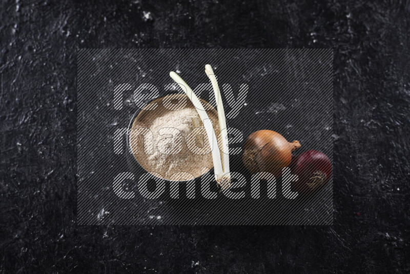 A black pottery bowl full of onion powder on black background