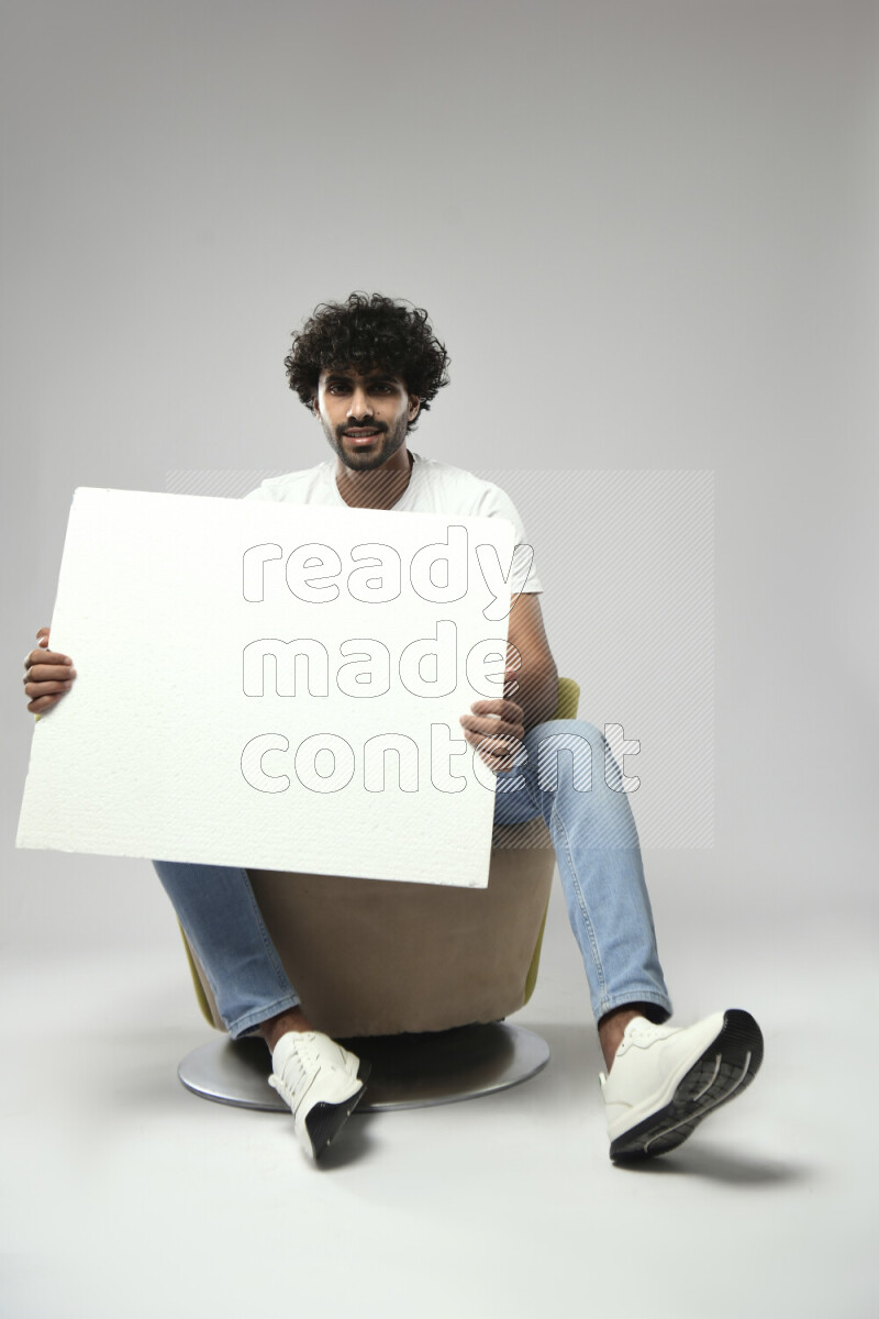 A man wearing casual sitting on a chair holding a white board on white background