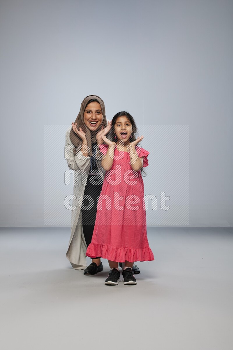 A girl and her mother interacting with the camera on gray background