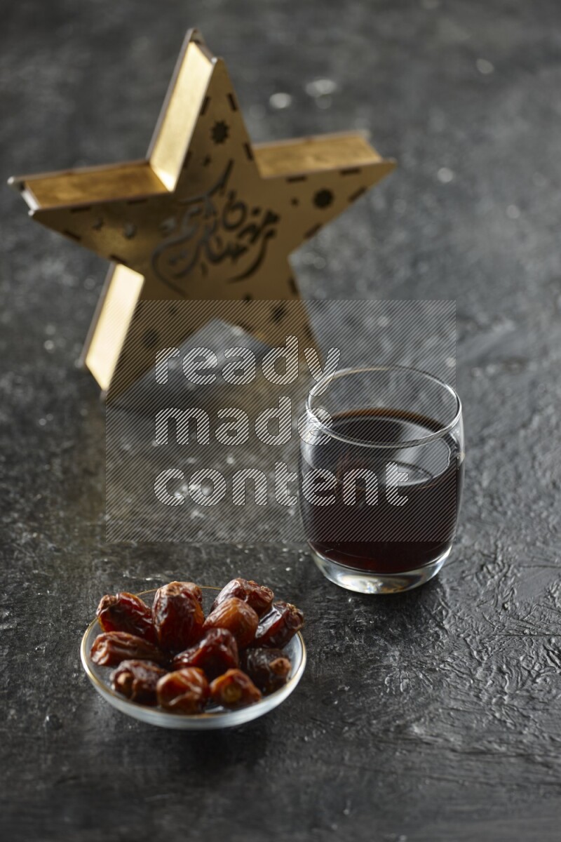 A wooden golden star lantern with different drinks, dates, nuts, prayer beads and quran on textured black background