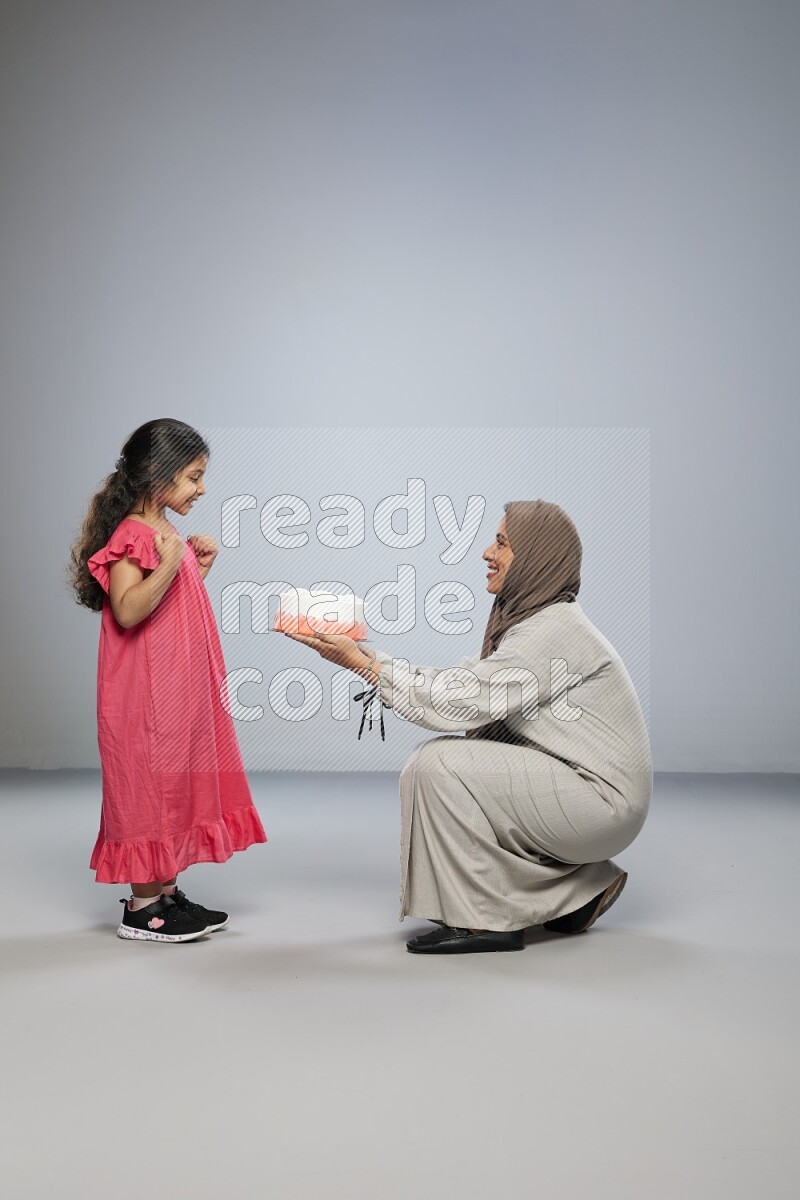 A mother giving a cake to her daughter on gray background
