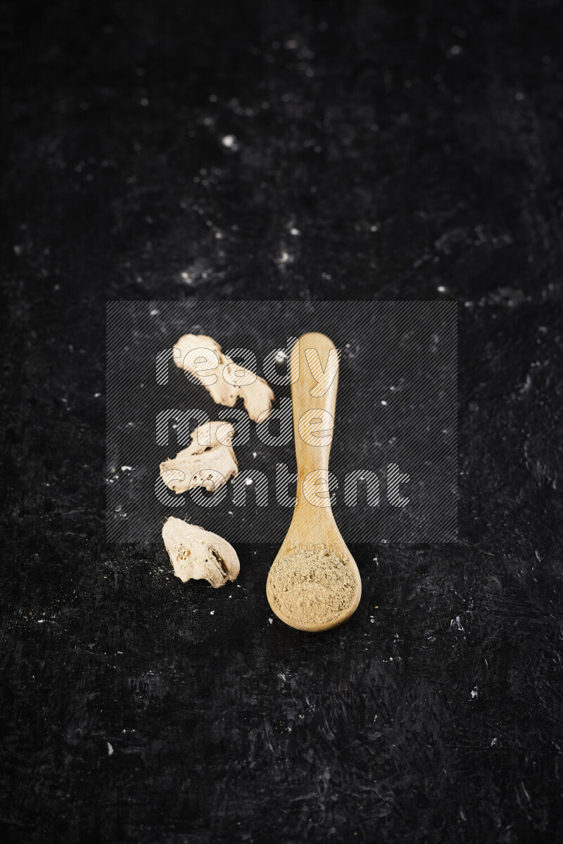 A wooden spoon full of ground ginger powder on black background