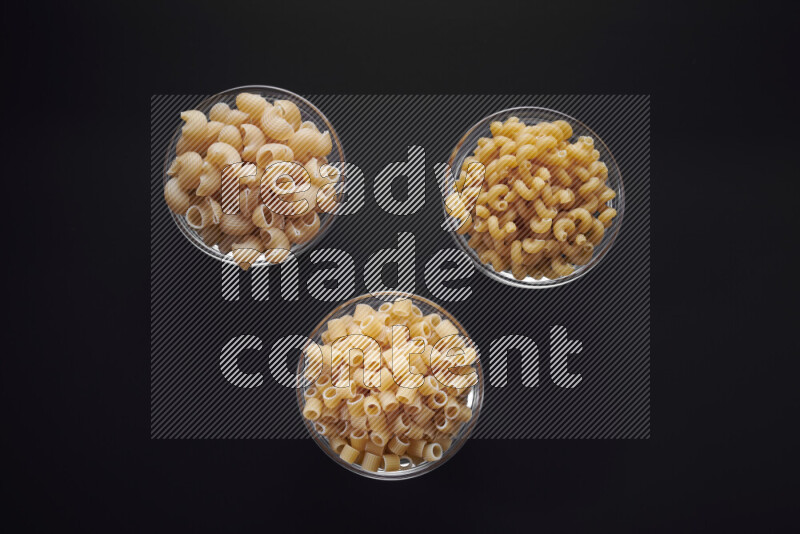 Different pasta types in glass bowls on black background