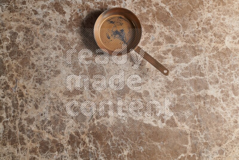 A small copper pan on beige marble background