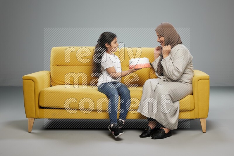 A girl sitting giving a cake to her mother on gray background