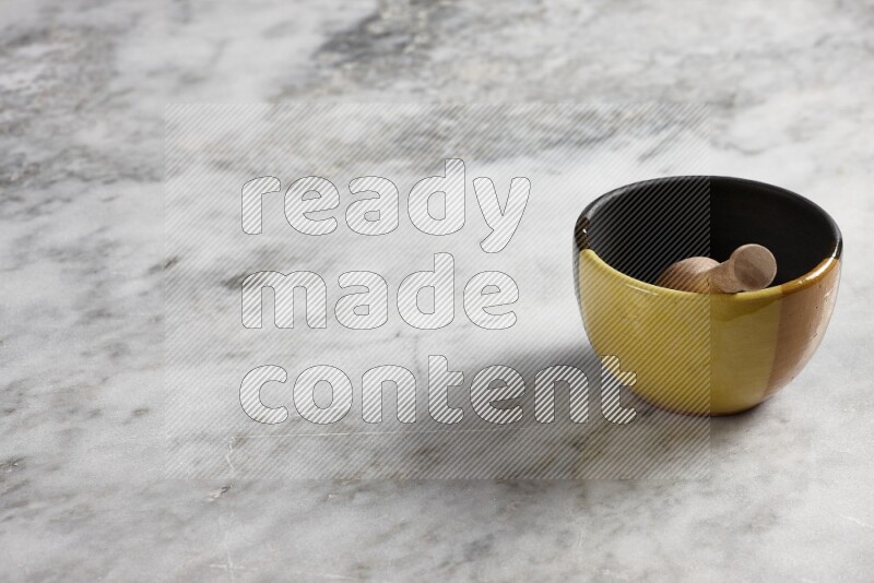 Multicolored pottery bowl with wooden honey dipper in it on grey marble background