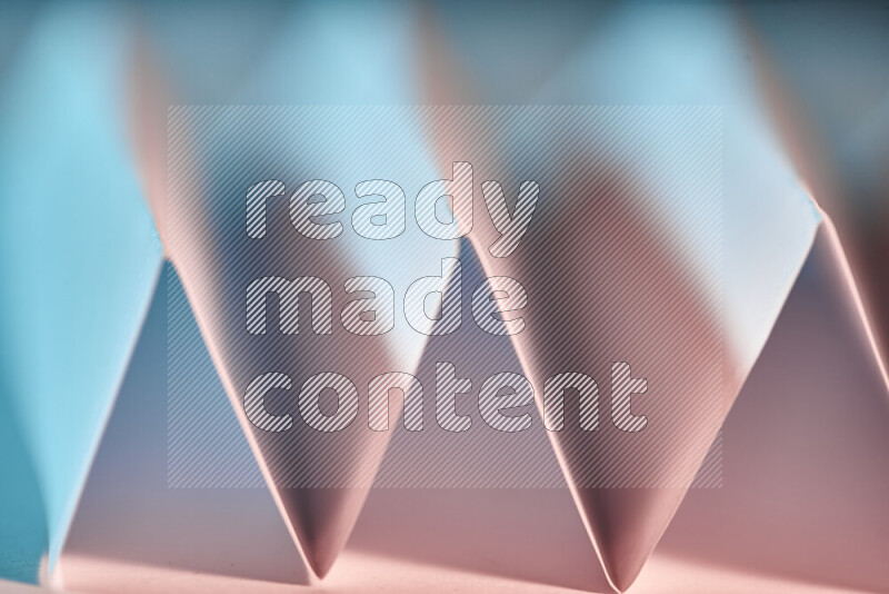 A close-up abstract image showing sharp geometric paper folds in blue and pink gradients