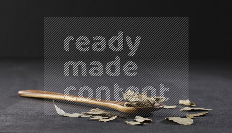 A wooden ladle filled with dried bay leaves on black flooring